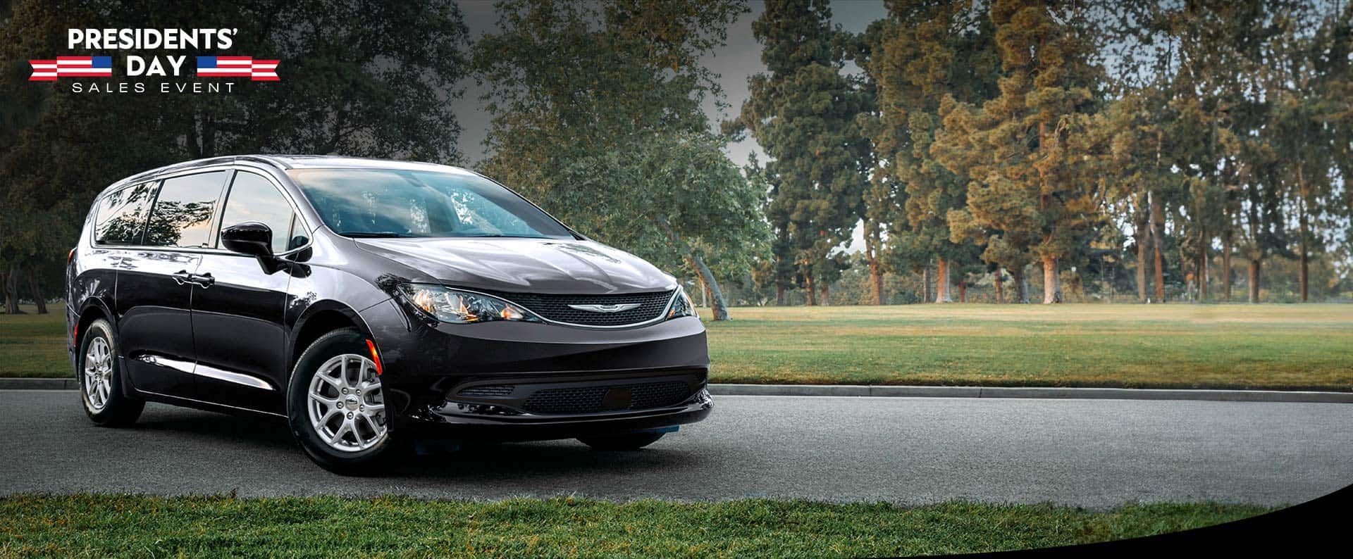 A front passengers side view of a black 2026 Chrysler Voyager LX in a parking lot of a park. Presidents' Day Sales Event.