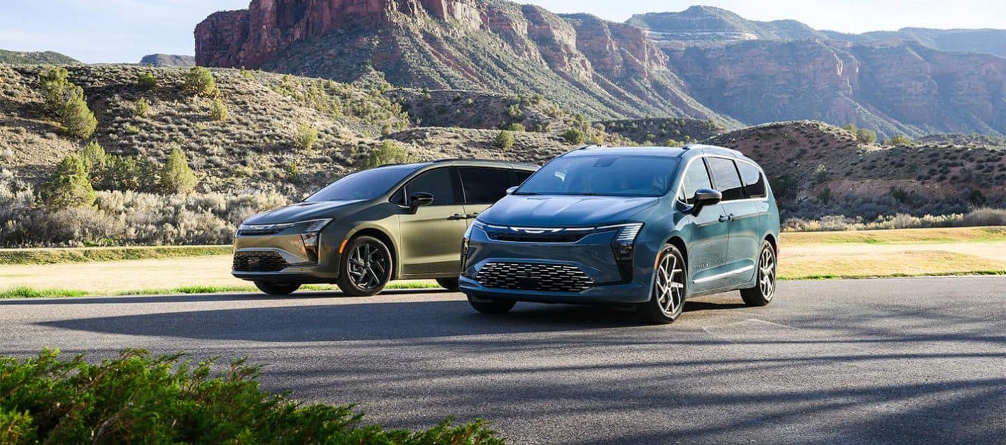 Display Two 2027 Chrysler Pacifica minivans parked opposite of each other--on the left an olive green Pacifica Limited with the S Appearance Package and a blue Pacifica Pinnacle on the right.