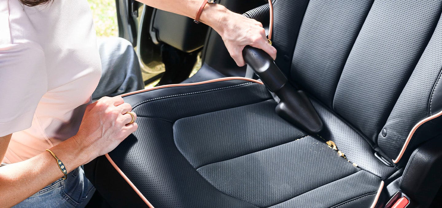 A close up of a woman standing at the open sliding side door of the 2027 Chrysler Pacifica, vacuuming the second-row carpeting with the integrated vacuum.