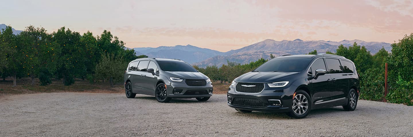A 2021 Chrysler Pacifica Limited and 2021 Chrysler Pacifica Hybrid Pinnacle, parked on a clearing in the mountains.