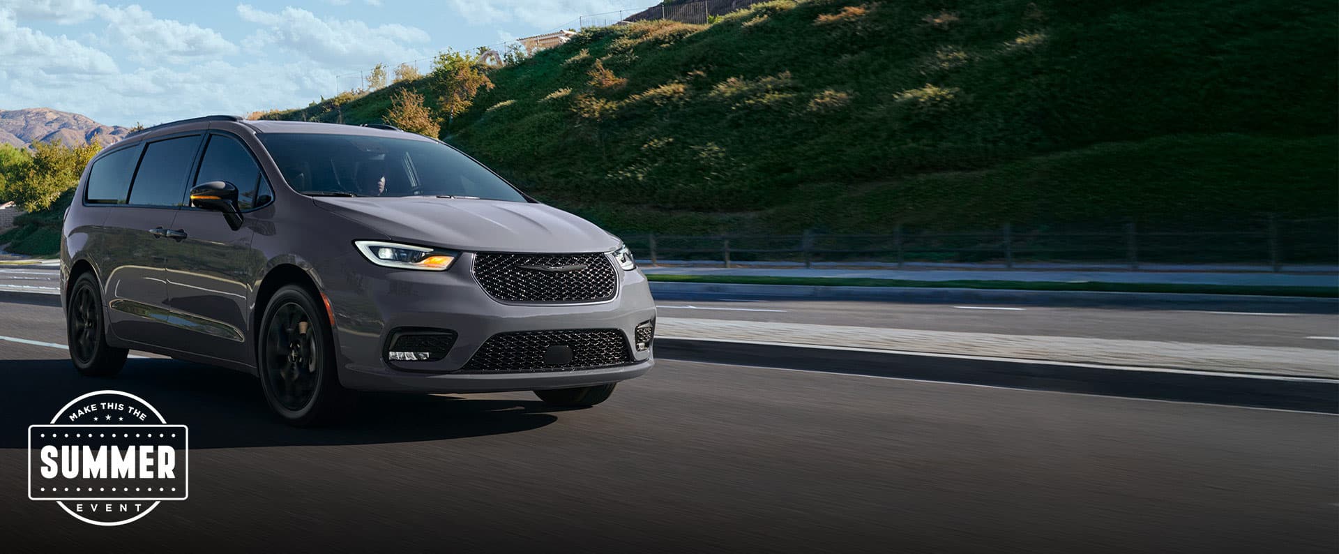 A light gray 2025 Chrysler Pacifica Limited traveling down a highway in the mountains. Make this the Summer sales event.