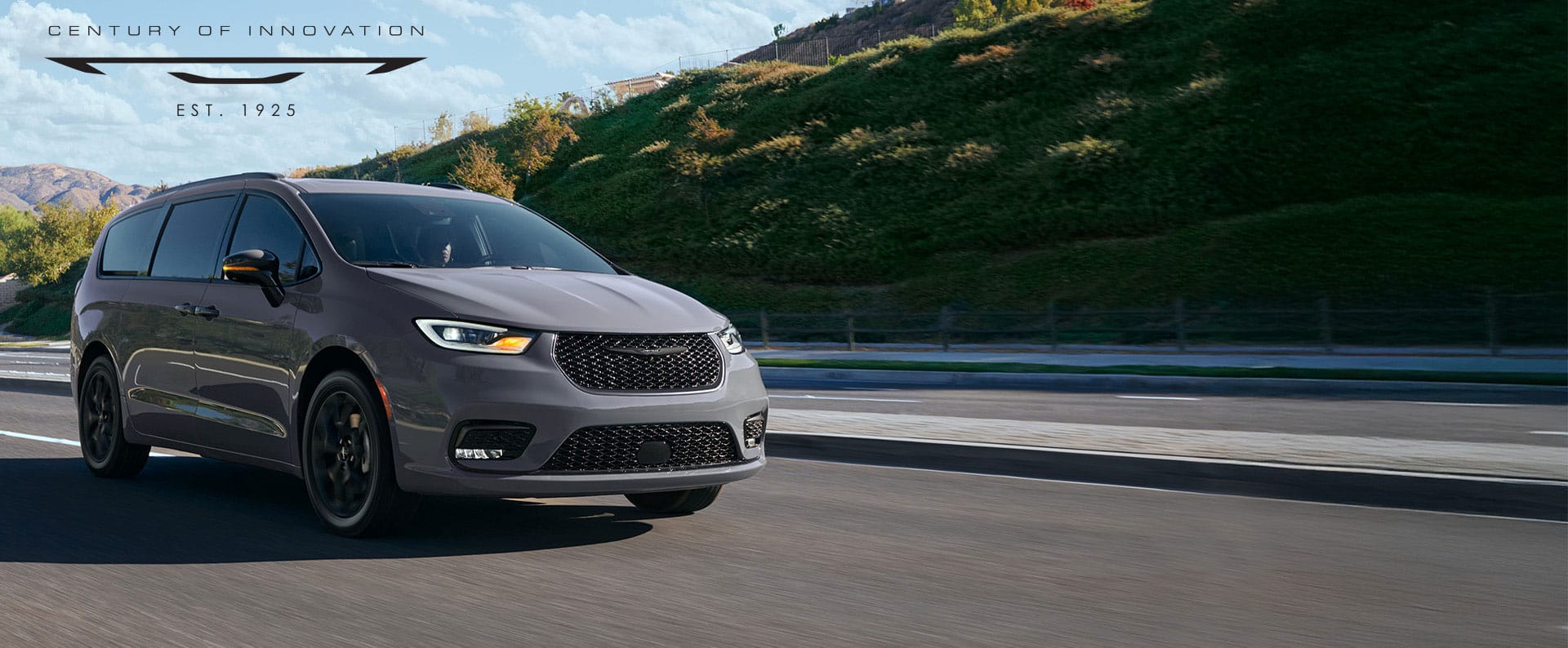 A light gray 2025 Chrysler Pacifica Limited traveling down a highway in the mountains. Century of Innovation.