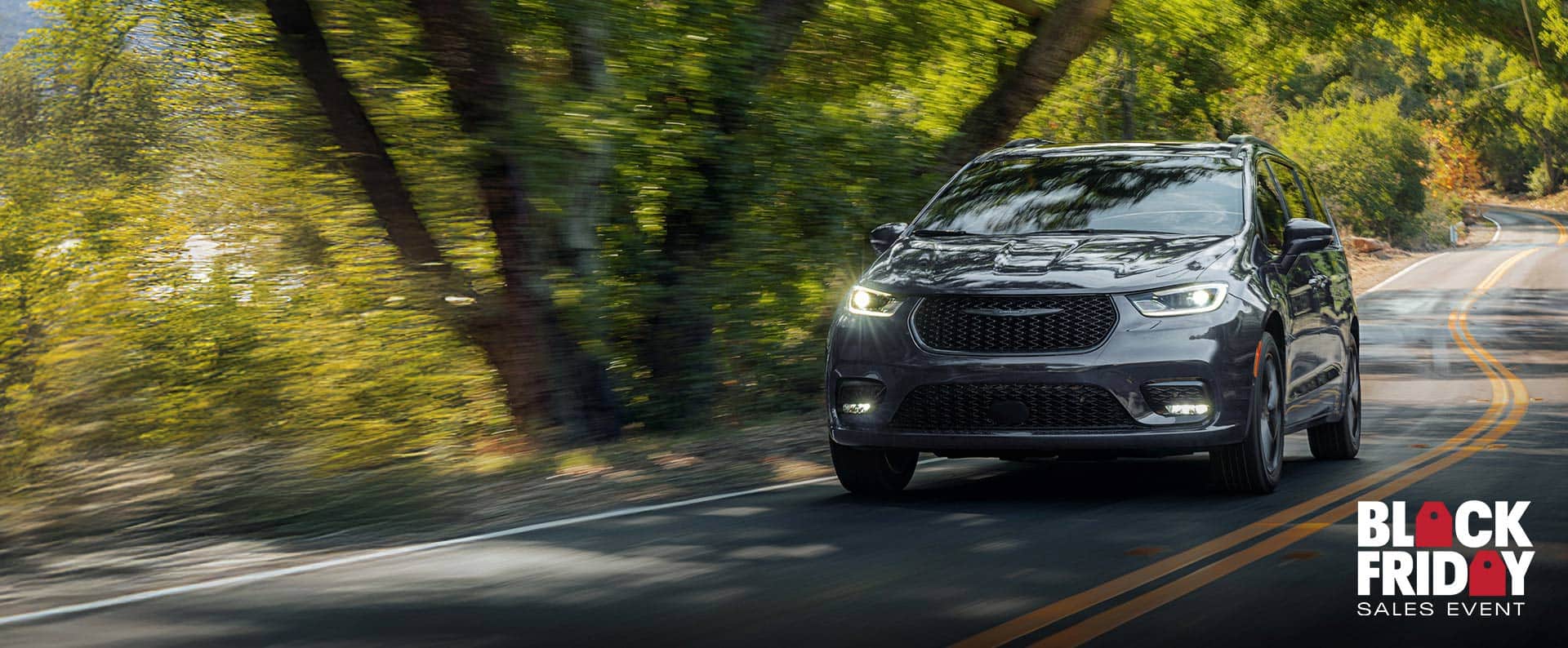 A gray 2026 Chrysler Pacifica Limited traveling down a winding highway in the woods. Black Friday Sales Event.