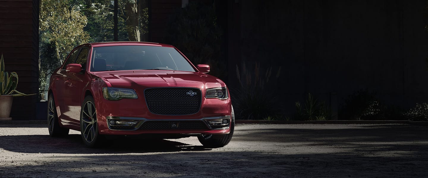 A front three-quarter view of a red 2023 Chrysler 300C parked in the driveway of a contemporary home.