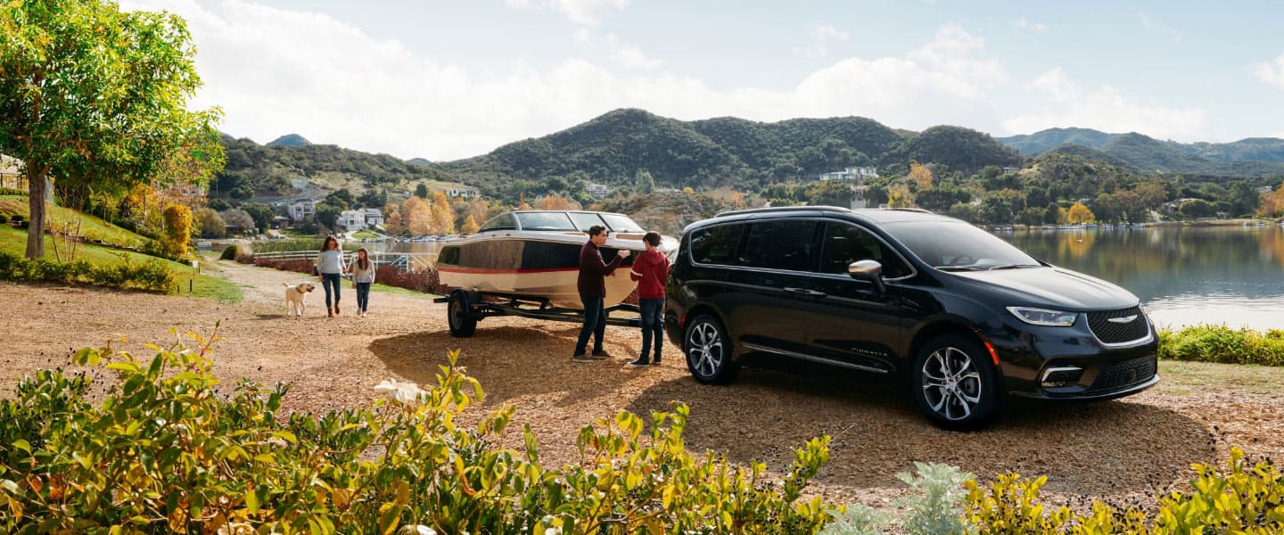 A woman carrying two baskets of apples swings her foot under the liftgate of a 2022 Chrysler Pacifica to open it as her family approaches with their own apple-picking baskets in hand.