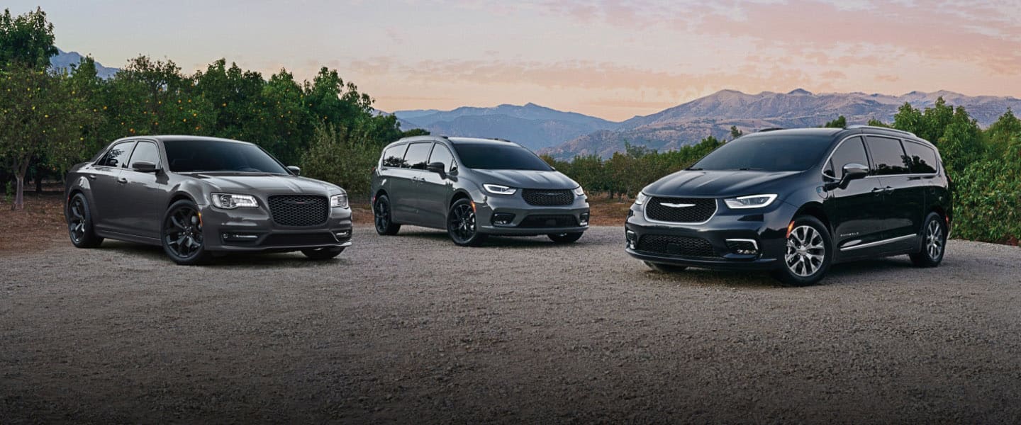 The 2022 Chrysler lineup parked on a clearing with mountains in the background: From left to right, the 2022 Chrysler 300S, Chrysler Pacifica Limited with the S Appearance Package and Chrysler Pacifica Hybrid Pinnacle.