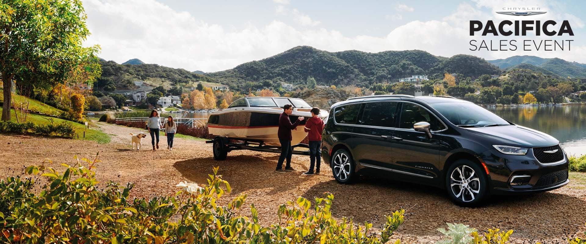 A passenger-side angle of a black 2024 Chrysler Pacifica Pinnacle gas model parked beside a lake, towing a motor boat, with a family of four and their dog nearby. Pacifica sales event.