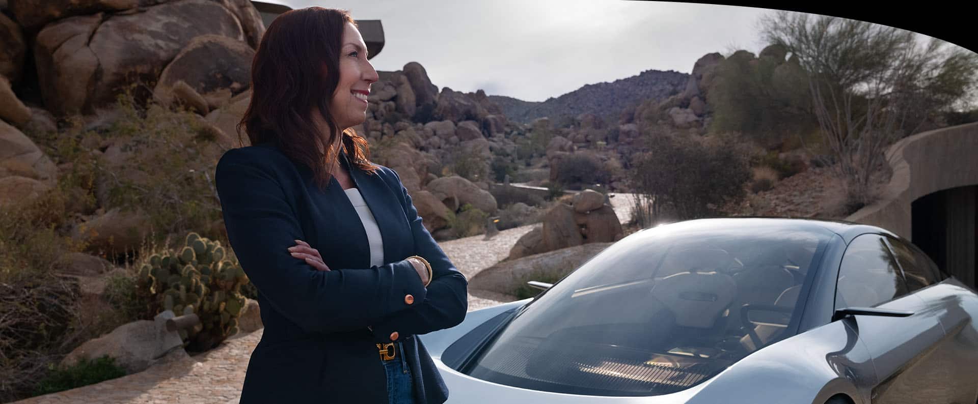 A woman standing in front of the Chrysler Halcyon concept vehicle parked near a tunnel in the mountains.