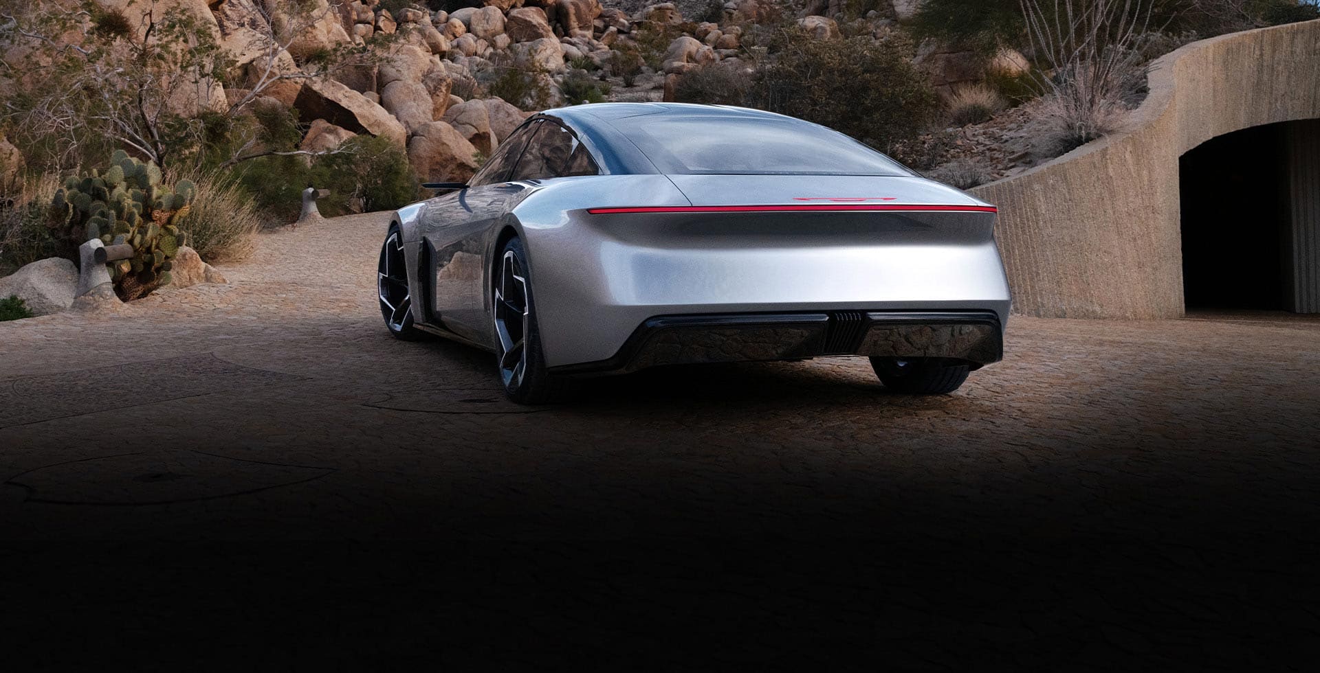A rear angle of the silver Chrysler Halcyon Concept vehicle parked on a clearing outside a tunnel, with rock formations in the background.