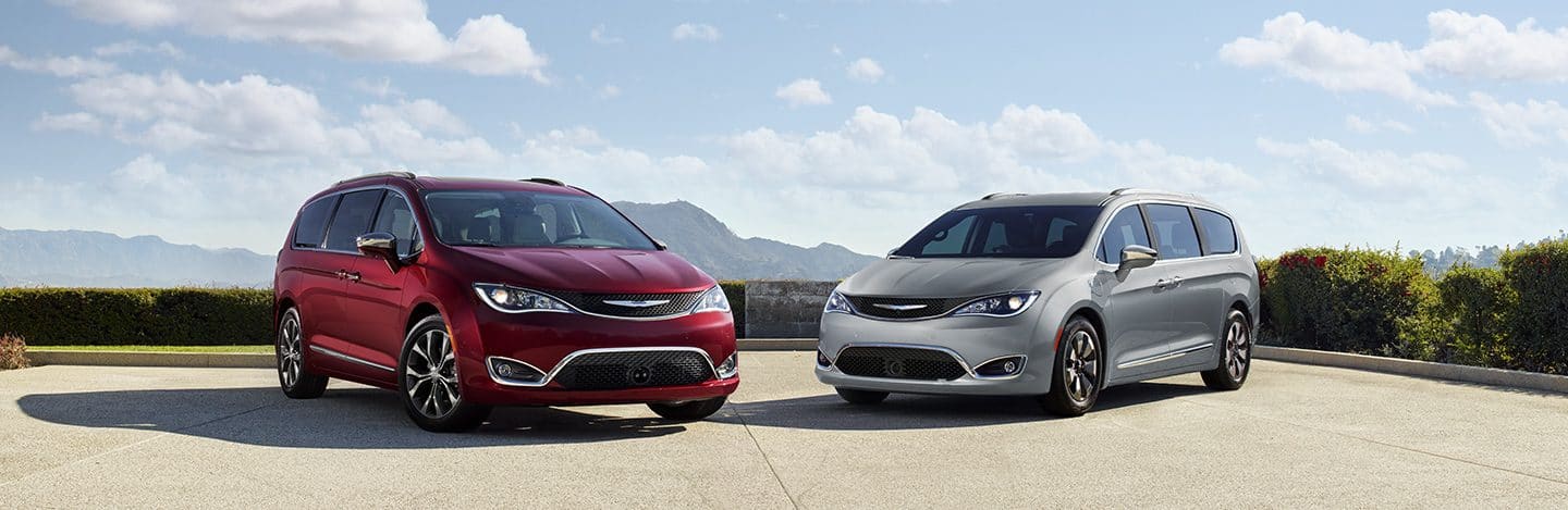 Front view of the Chrysler Pacifica in Red and the Chrysler Pacifica Hybrid in Silver parked and angled toward one another.