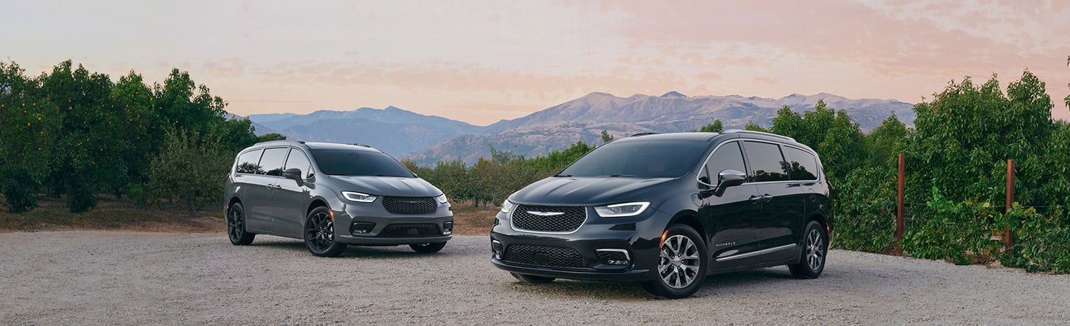 A 2021 Chrysler Pacifica Limited and 2021 Chrysler Pacifica Hybrid Pinnacle, parked on a clearing in the mountains.