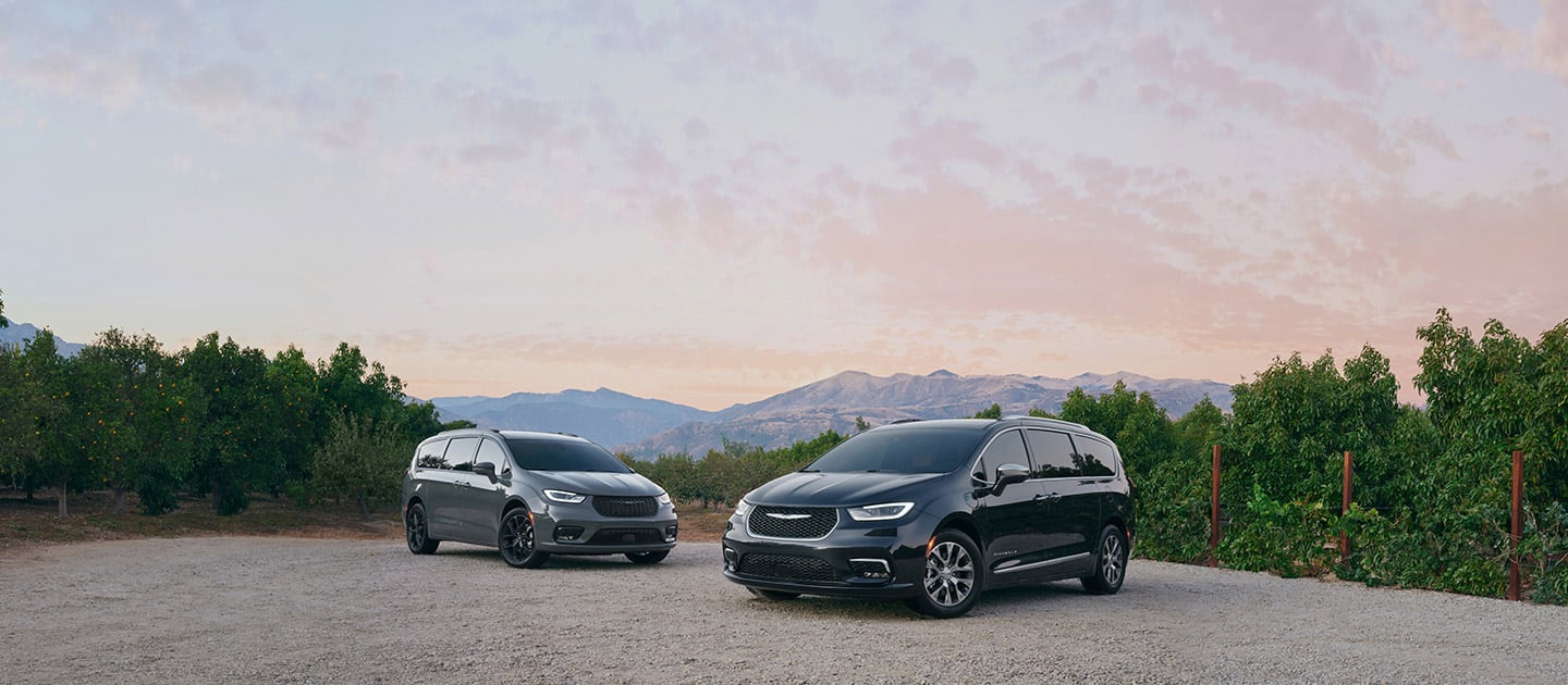 A 2021 Chrysler Pacifica Limited and 2021 Chrysler Pacifica Hybrid Pinnacle, parked on a clearing in the mountains.