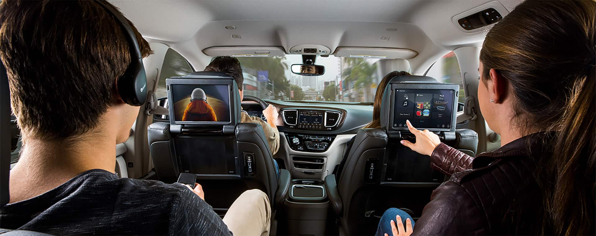 Two passengers in the second row of a 2021 Chrysler Pacifica Limited using the dual touchscreens mounted on the back of the front seats.
