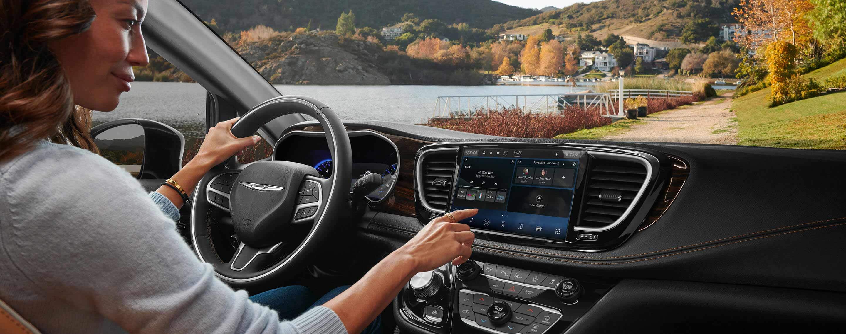 The driver in a 2021 Chrysler Pacifica Limited with one hand on the wheel and the other making a selection on the Uconnect touchscreen.