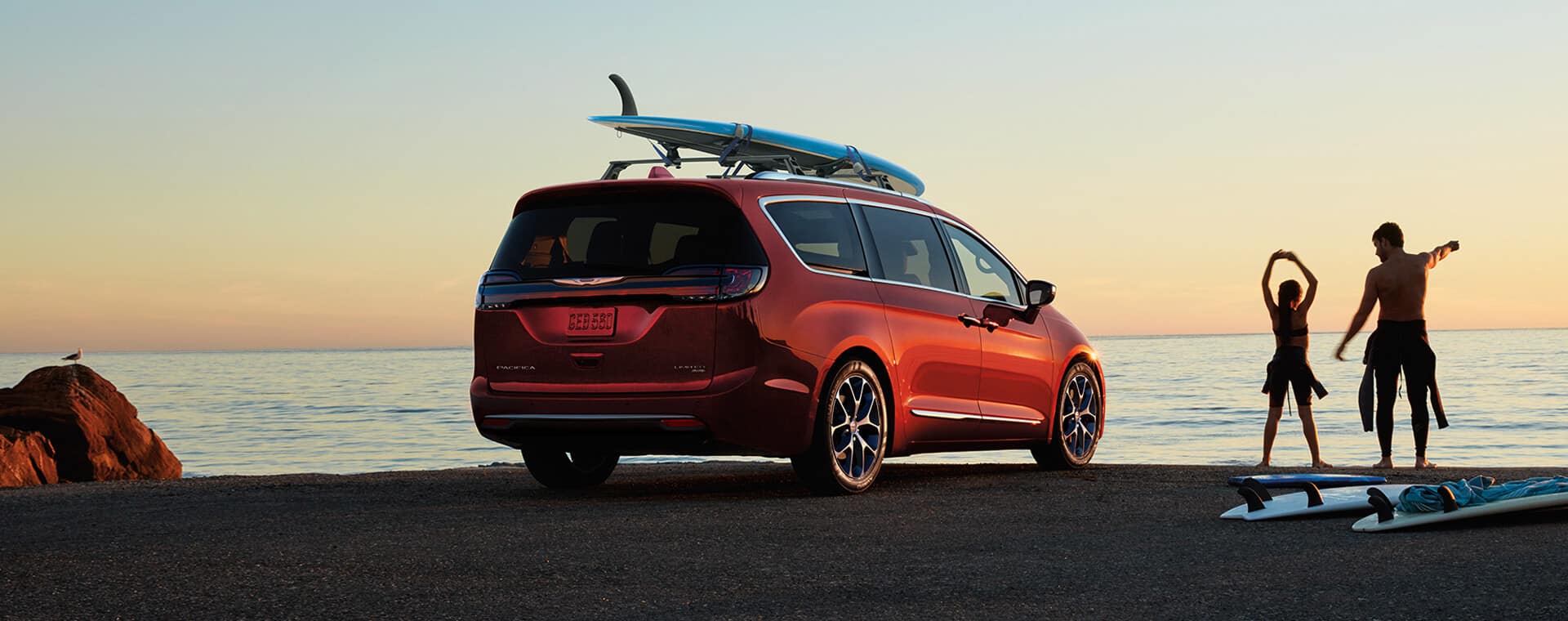 A red 2021 Chrysler Pacifica Limited parked at the beach with a kayak strapped to it's roof rack.