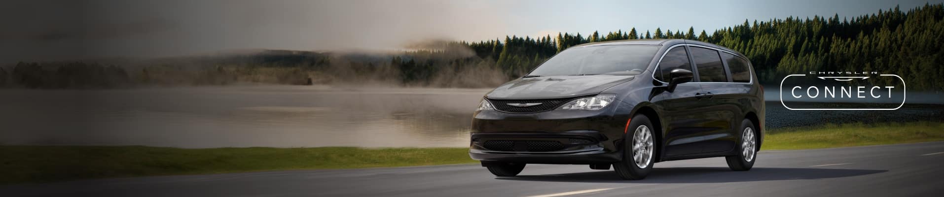 A driver-side front angle of a black 2026 Chrysler Voyager traveling on a highway with a forest in the background. The Chrysler Connect logo.