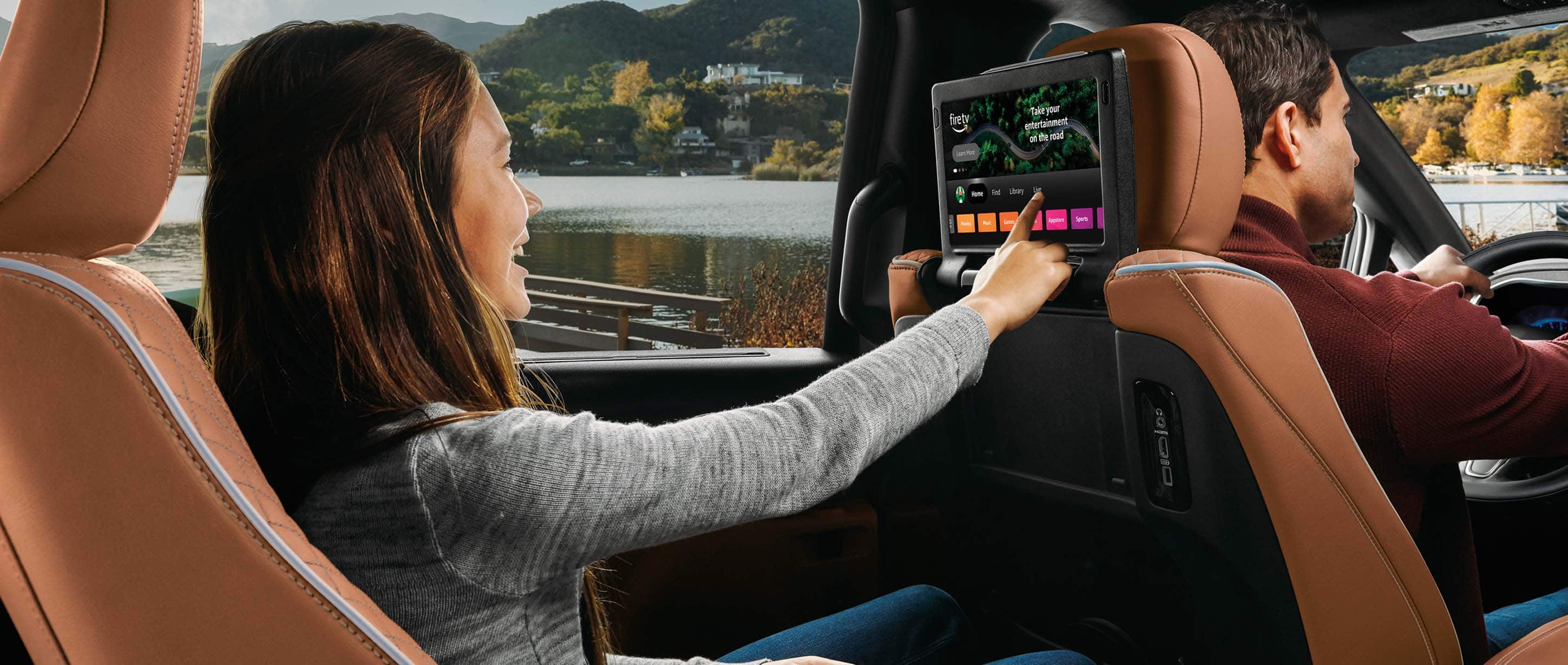 The second row of the 2024 Chrysler Pacifica Pinnacle, with a young girl making a selection on the Amazon Fire TV page displayed on the touchscreen that is mounted on the back of the driver seat.